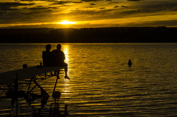 Couple sitting at the end of a dock at sunset