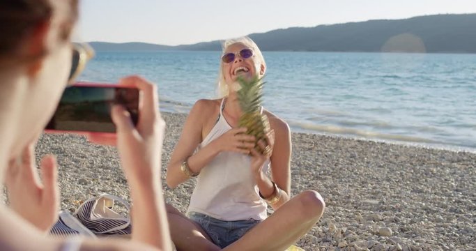 Close up attractive woman holding up pineapple posing for camera smiling laughing pretending to eat fruit at sunset on tropical beach