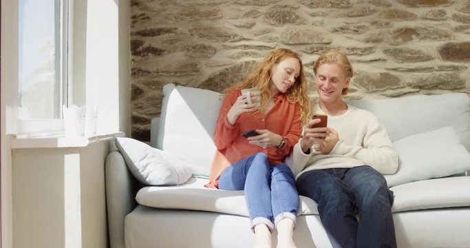 Beautiful redhead woman sharing photos with boyfriend using smartphone couple engaged in technology at home touching screen browsing social media for authentic creative content