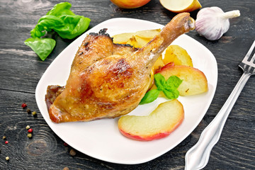Duck leg with apple and potatoes on black board