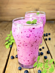 Milkshake with blueberries in two glasses on board