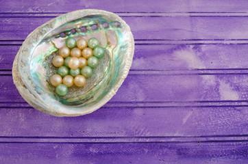 A mother of pearl shell with bath beads on a purple background with copy space