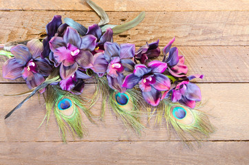 Maroon silk orchids and peacock feathers on a rustic wood background