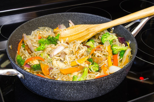 Chicken and vegetable chop suey in a ceramic coated pot on a glass cooktop