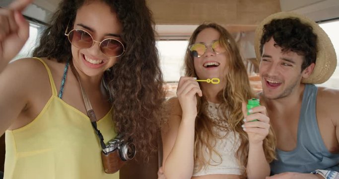Portrait Beautiful Teenage hipster friends blowing soap bubbles having fun at festival in camper van on road trip adventure