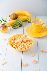 Healthy breakfast with cereal flakes and fruit near vase with flowers on white background. Yellow tone