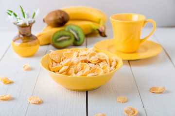 Healthy breakfast with cereal flakes and fruit near vase with flowers on white background. Yellow tone