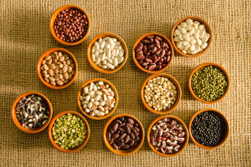 12 pottery containers with various types of pulse and legume seeds on a burlap background.