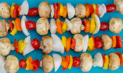 Fresh vegetable kebabs on a blue mat ready to grill