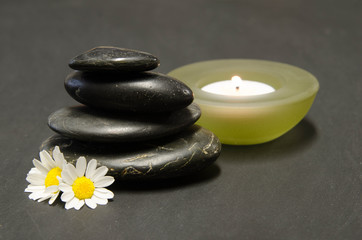 Spa arrangement with black stones and white daisies and a burning candle on a black background