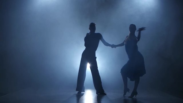 Dance cha-cha-cha performed by professional couple in smoky studio, silhouette