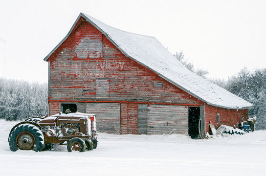 Vintage tractors in front of an old red barn in snow