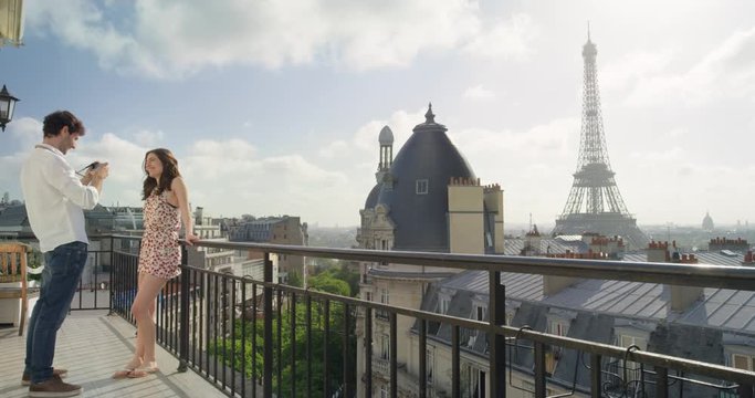 Tourist couple taking photograph of Eiffel Tower using smartphone from hotel balcony at sunrise photographing scenic Paris cityscape background view enjoying European honeymoon vacation travel adventure