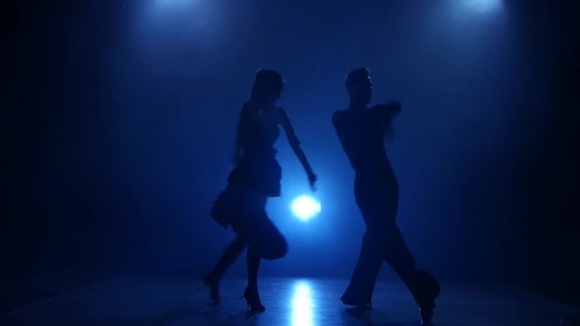 Silhouette of pair dancers performing latino dance in smoky studio