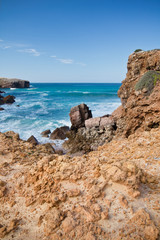 picturesque atlantic coast cliffs rocks with breaking waves in colorful blue sky, algarve, portugal