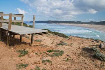 broken wooden pathway with stunning overhanging view on beautiful atlantic coast with beach of bordeira from cliff ledge, popular surf destination in algarve, portugal