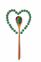 Wooden spoon with spirulina tablets in the center of the heart of round spirulina tablets 