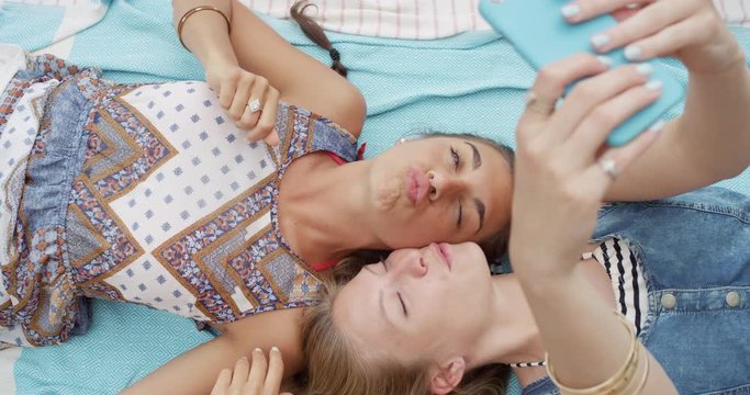 Top view of teenage girl friends taking selfie photo with smart phone lying on back smiling laughing at beach direct from above