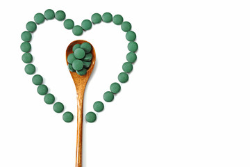 Wooden spoon with spirulina tablets in the center of the heart of round spirulina tablets on a white background