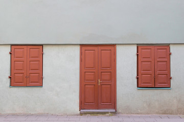 Facade of the old house with wooden door and two closed windows.