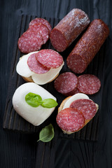Salami and mozzarella bruschettas over black wooden background, studio shot