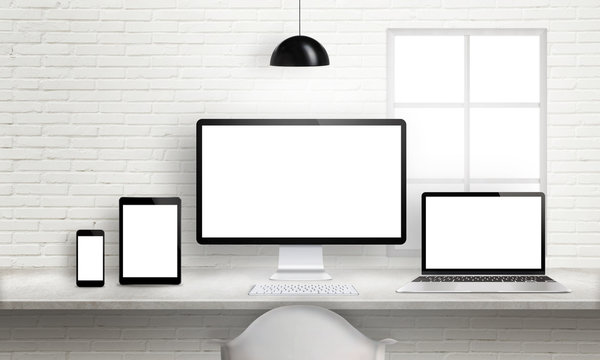 Multiple devices on office desk for responsive web site design presentation. Brick white wall in background.
