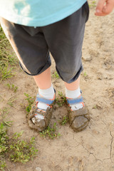 a young boy child in sandals dirty with mud and water
