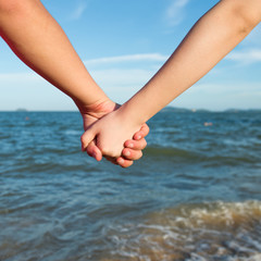 Summer couple holding hands in front of the sea.