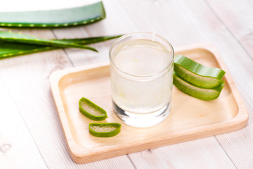 Glass of aloe vera juice with fresh leaves on a wooden table