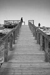 Obraz premium visiting, sightseeing and going up to the point of view on wooden pathway by the atlantic ocean in black and white, algarve, portugal