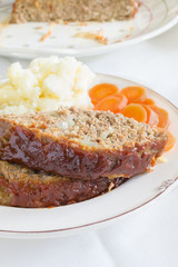 Classic American meatloaf made with ground beef oatmeal onions and a ketchup brown sugar and mustard glaze served with mashed potatoes and carrot coins