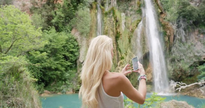 Woman taking photograph of secret waterfall with smartphone photographing scenic landscape nature background view enjoying vacation travel adventure