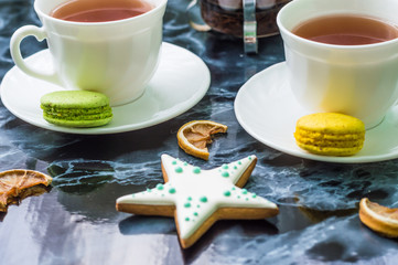 Still life with gingerbread nad macarons and tea on the black marble background