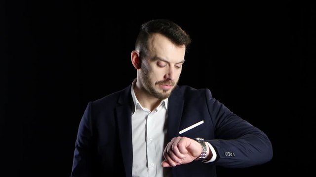 Businessman nervously waits and looks at his watch. Black background