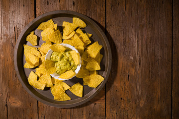 Nachos chips with salsa guacamole on a platter over an old wooden table