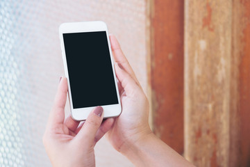 Mockup image of hand holding white mobile phone with blank black screen and vintage glass mirror background   