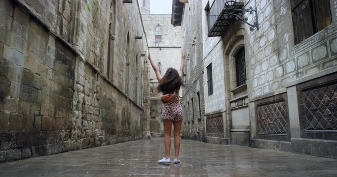 Happy young woman dancing freestyle in European City wearing summer dress in rainy weather celebrating travel adventure