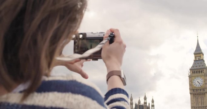 Tourist woman taking photo of Big Ben London with vintage camera for social media at sunset enjoying vacation travel adventure