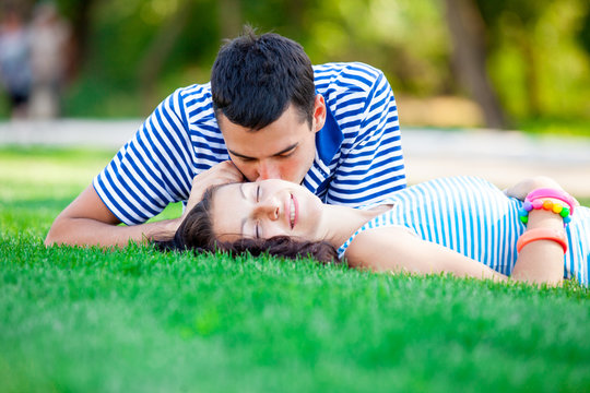 photo of cute couple kissing and lying on the grass in the field