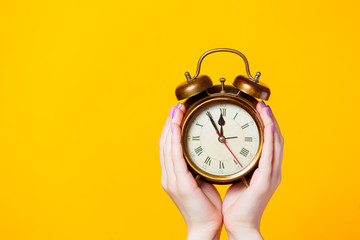 photo of female hands holding alarm clock on the wonderful yellow background