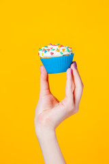 photo of female hand holding cupcake on the wonderful yellow background