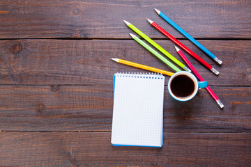 photo of notebook with pencil, cup of coffee and colorful pencils on the wonderful brown wooden background