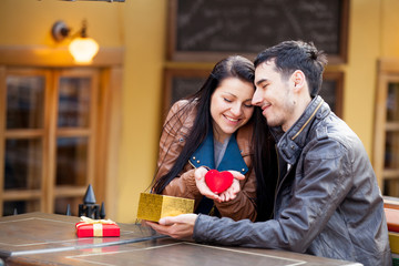 photo of cute couple sitting on the bench and holding heart shaped toy on the wonderful cafe background
