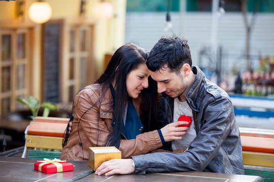 photo of cute couple sitting on the bench and holding heart shaped toy on the wonderful cafe background