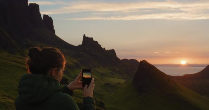 Woman taking photograph  sunset with smartphone photographing scenic landscape nature background view enjoying vacation travel adventure Quiraing Walk on the Isle of Skye in Scotland