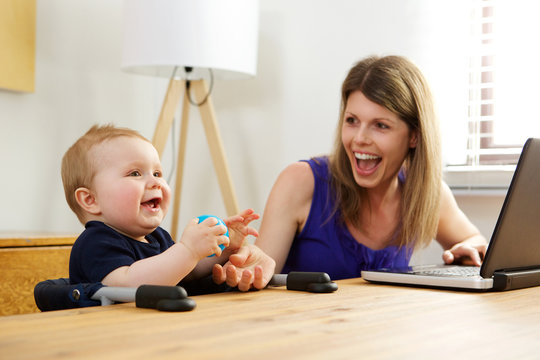 single mother working on laptop with her baby boy at home
