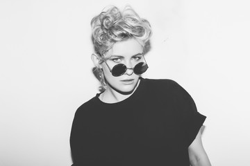 Stylish fashion sexy blonde bad girl in a black t-shirt and rock sunglasses. Dangerous rocky emotional woman. white toned. background, not isolated