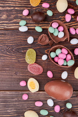 Wooden background with candies. Broken chocolate egg and sweets.