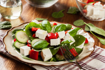 Fresh spinach salad with feta, cucumber and red paprika on a plate.