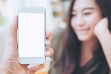 Mockup image of hand holding white mobile phone with blank white screen and blur smiley woman face background in modern cafe